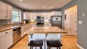 Une cuisine avec des meubles blancs, un îlot central, des appareils électroménagers en acier inoxydable et un plancher en bois.