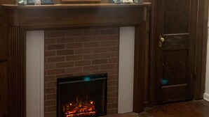 Una chimenea con revestimiento de ladrillo y puerta de cristal, flanqueada por paneles de madera con dos apliques de pared.