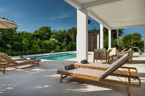 Zona junto a la piscina con sillones de descanso, un espacio cubierto para sentarse y vistas a una piscina.
