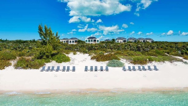 Propiedad frente a la playa con varias villas, una playa de arena y aguas turquesas cristalinas.