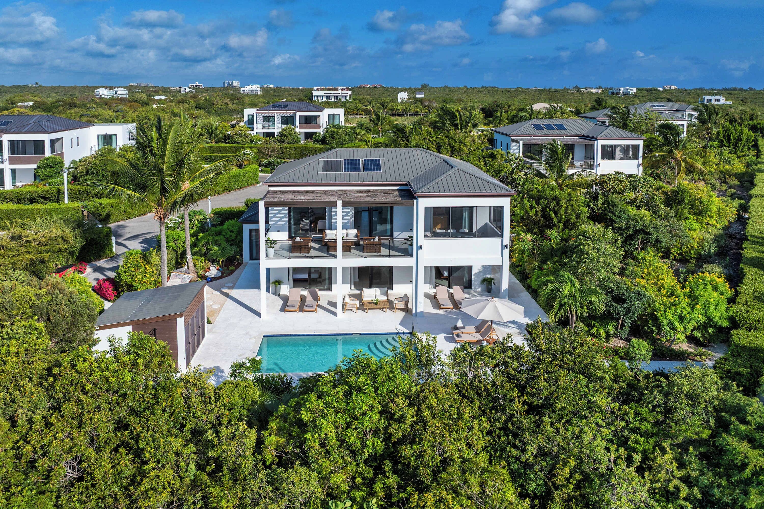 A two-story house with a large balcony, a swimming pool, and lush greenery surrounding the property.