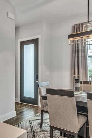 Comedor con una mesa dispuesta para cuatro, una lámpara colgante moderna y vistas al exterior a través de una puerta.