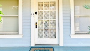 Una casa con puerta blanca, felpudo que dice 'HOME' y ventana con persianas.