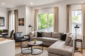 A modern living room with a sectional sofa, a round coffee table, and a dining area with a table and chairs.