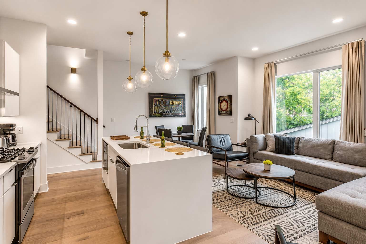 A modern kitchen with a central island, a dining area with a sofa and coffee table, and a living room with a large window.