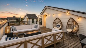 Une terrasse sur le toit avec un canapé blanc, deux fauteuils en osier, un foyer et des guirlandes lumineuses.