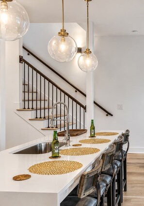 A modern kitchen with a central island, stainless steel sink, and a bar area with stools.