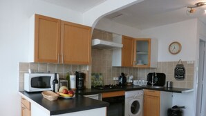 A compact kitchen with wooden cabinets, a microwave, a washing machine, and a coffee maker. - Gite1 T3 with swimming pool in the heart of the vineyards (34310 - CAPESTANG)