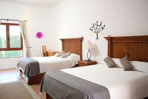 Habitación de hotel con dos camas, cabecero de madera, mesita de noche con lámpara, decoración en la pared y ventana con cortinas.
