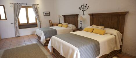 Une chambre d’hôtel avec deux lits, une tête de lit en bois, une table de chevet, une lampe, une fenêtre avec des rideaux, un tapis et un élément décoratif mural.