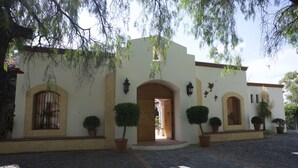 A building with a white facade, arched doorways, and potted plants. - La Casona de los Colibríes (Corregidora)