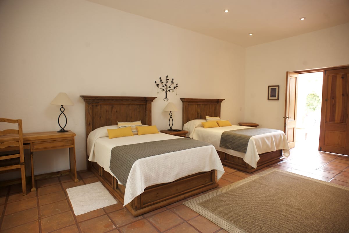 A bedroom with two beds, a wooden desk, a chair, a nightstand, and a wall-mounted lamp.