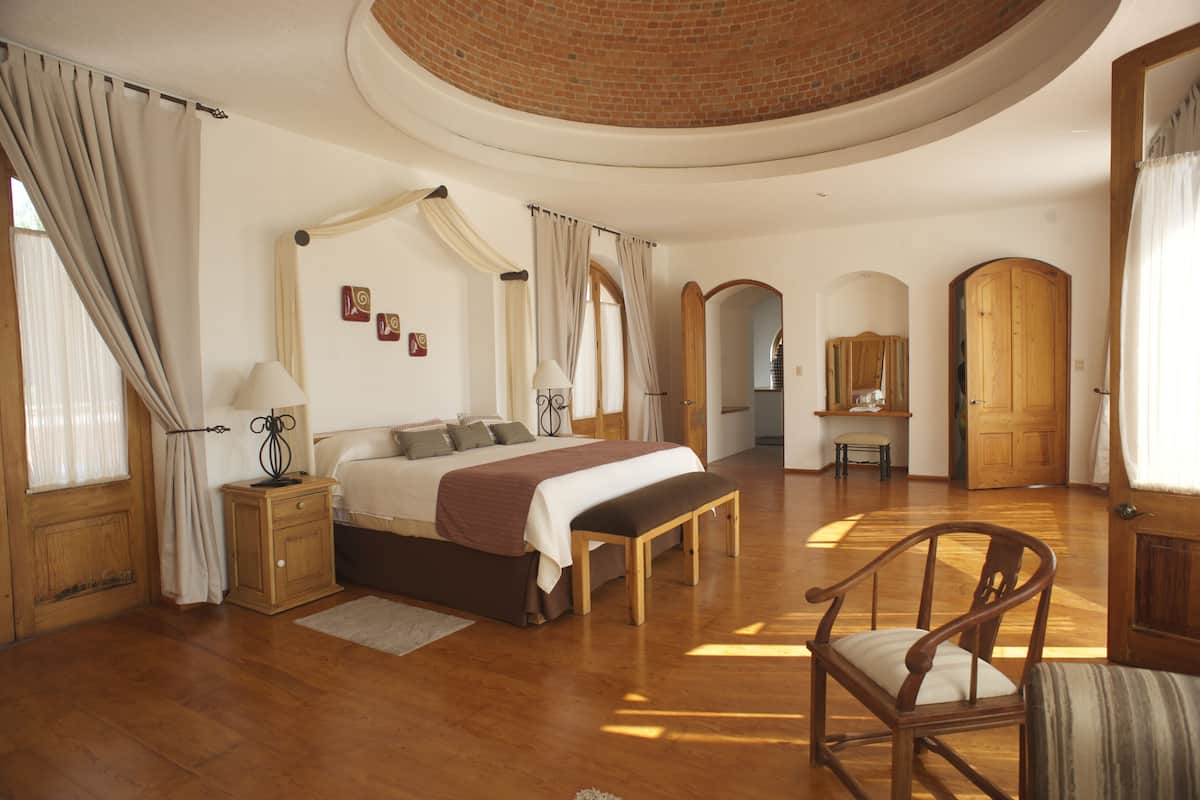 A spacious bedroom with a large bed, wooden furniture, and a curved ceiling.