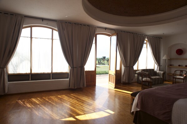 Una habitación amplia con ventanas grandes, una cama, una silla y una mesita.