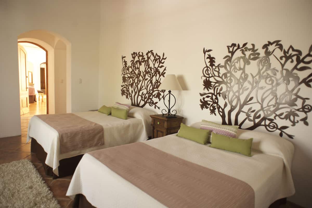 A hotel room with two beds, a nightstand, a lamp, and decorative wall art.