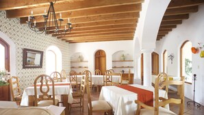 A dining area with wooden tables and chairs, a chandelier, and arched windows. - La Casona de los Colibríes (Corregidora)
