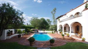 A swimming pool surrounded by a patio with potted plants and outdoor furniture. - La Casona de los Colibríes (Corregidora)
