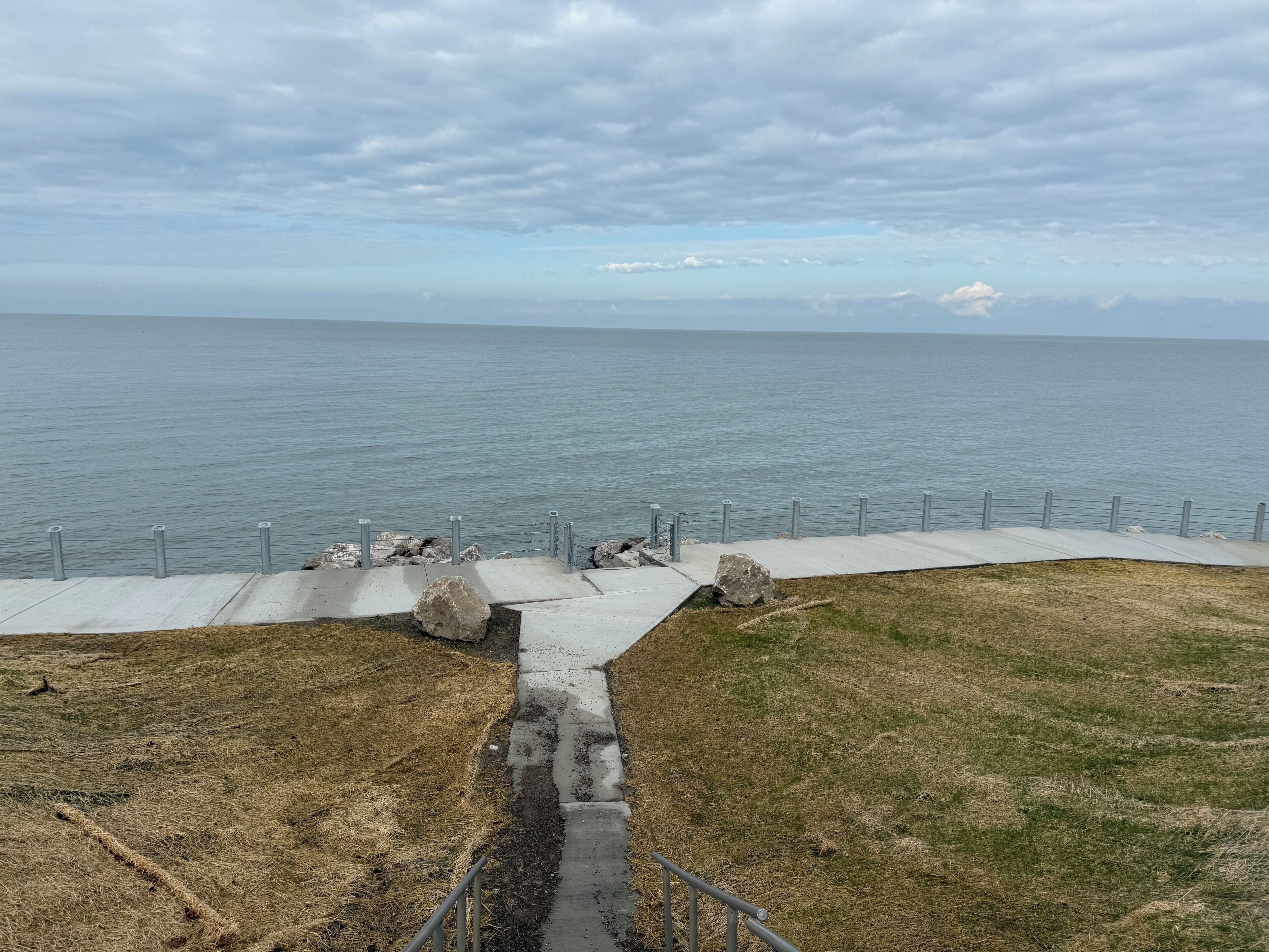 A coastal walkway with a concrete path, metal railings, and large rocks.