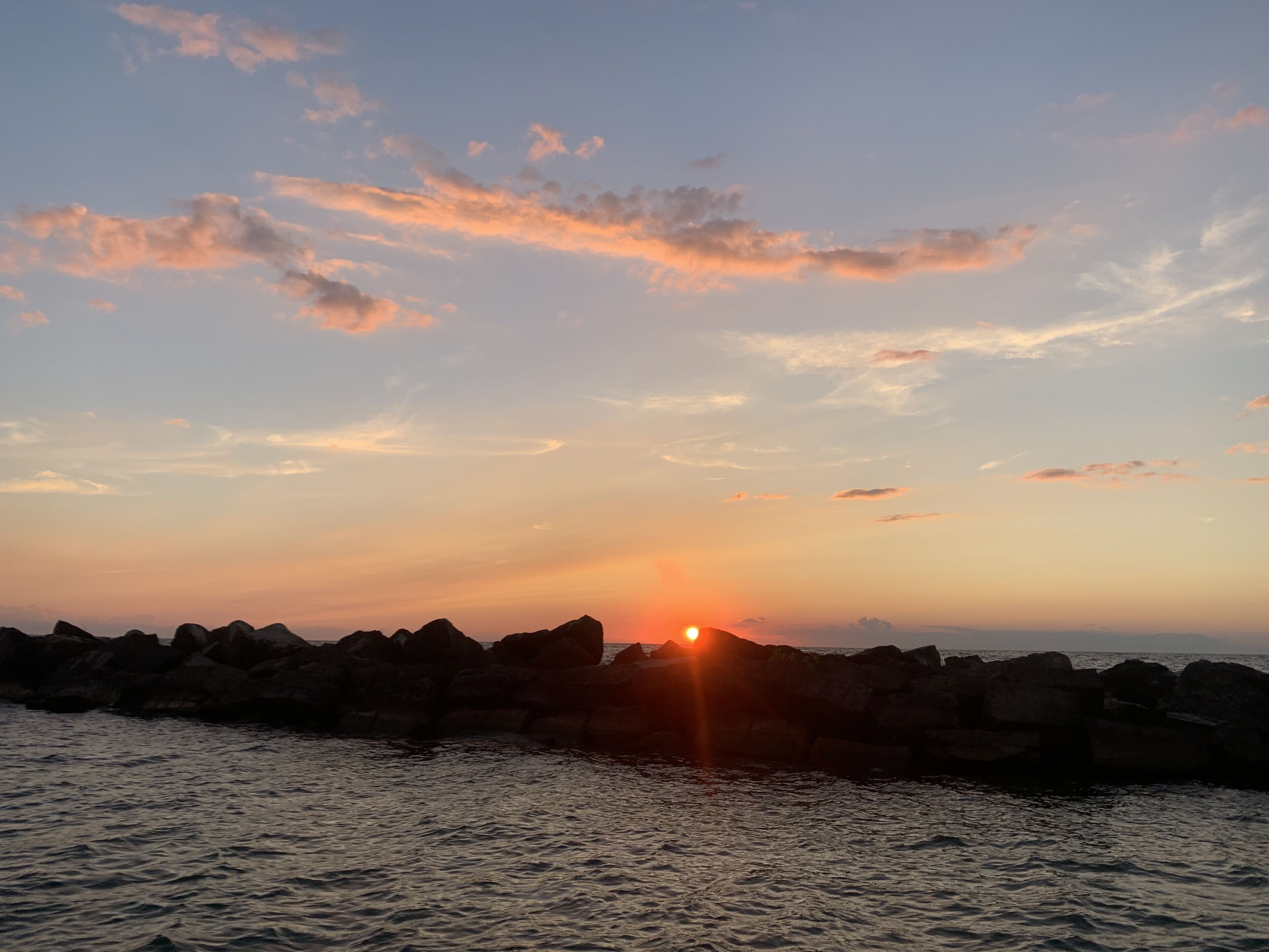 A sunset over a rocky coastline with calm waters.