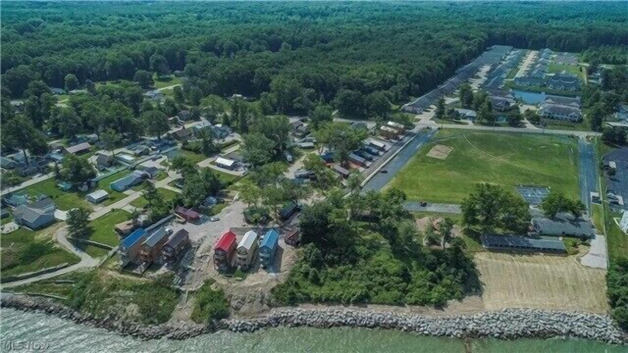 An aerial view of a residential area with houses, a sports field, and a rocky shoreline.