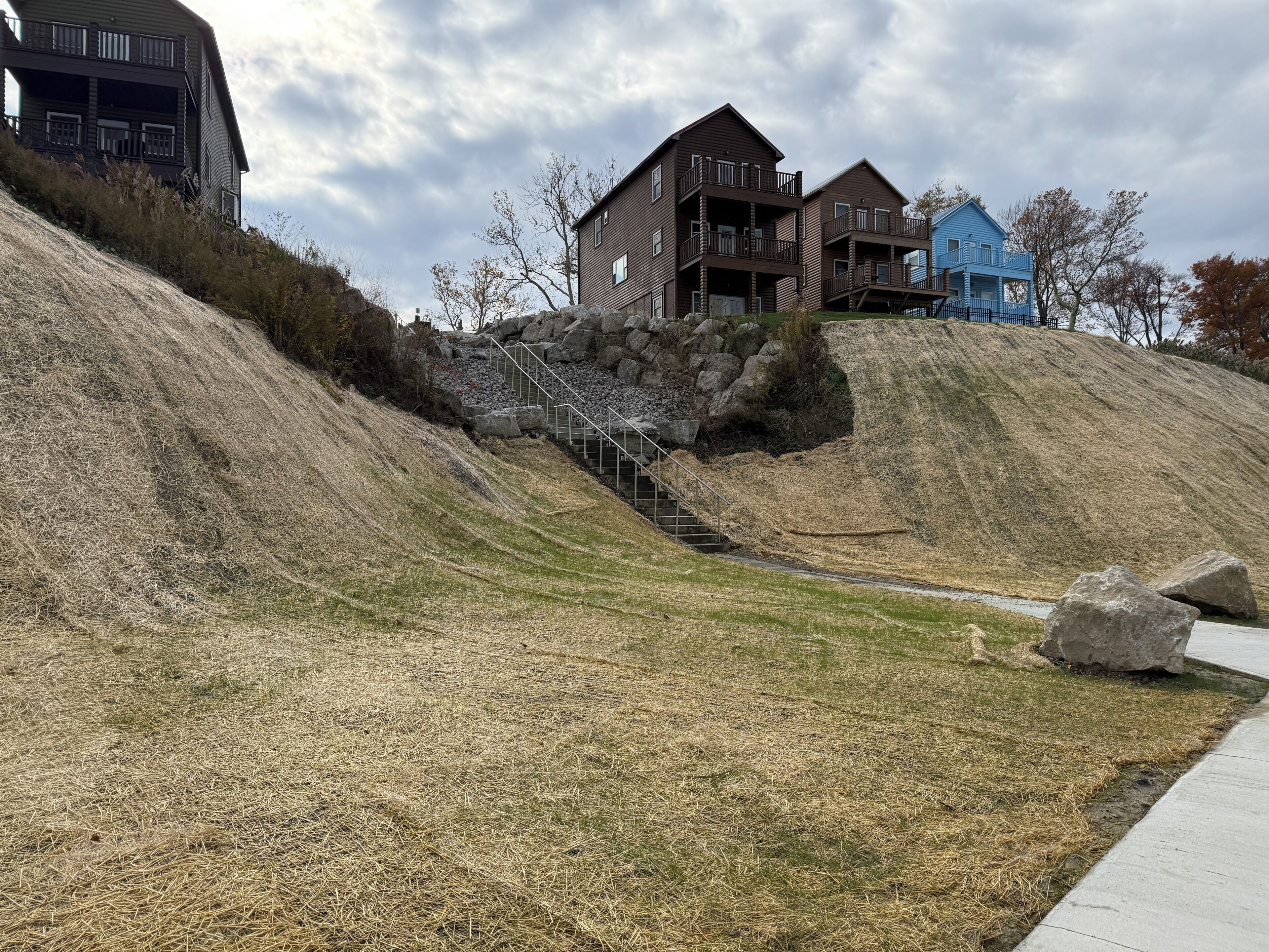 A residential area with a grassy slope, a staircase leading up to a building, and a paved path.