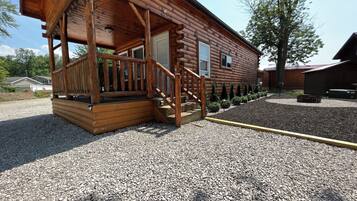 A wooden cabin with a porch, a gravel driveway, and a small garden area.