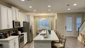 A modern kitchen with white cabinetry, stainless steel appliances, and a central island with seating. - Late Summer at Solara • Private Pool• Walk To Clubhouse (Kissimmee)