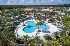 Un resort con una amplia piscina central, rodeado de palmeras y sillones de descanso.