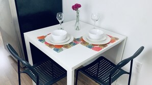 Una pequeña mesa de comedor con dos cuencos blancos, dos copas de vino y un florero con una sola flor.