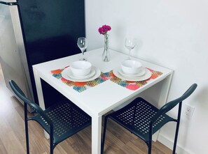 Une petite table à manger avec deux bols blancs, deux verres à vin et un vase contenant une seule fleur.