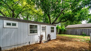A single-story house with a front porch, a small garden area with potted plants, and a wooden fence in the background. - Tiny house in Bishop Arts! (Dallas)
