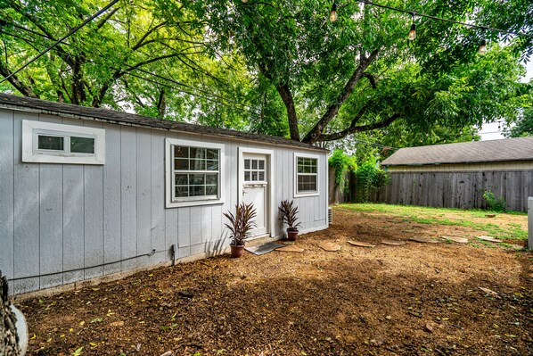 A single-story house with a front porch, a small garden area with potted plants, and a wooden fence in the background.