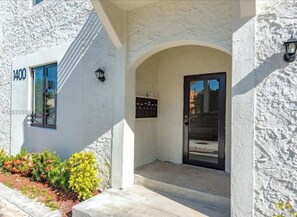 A building with a white stucco exterior, a black-framed door, and a small window with a number '1400' on the wall. - Super Cozy 1Brm Apartment in the Heart of Miami!! #7 (Miami)