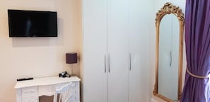 A bedroom with a TV, wardrobe, vanity, and a mirror.