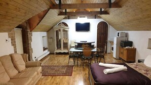 Ein gemütliches Schlafzimmer im Dachgeschoss mit Holzbalkendecke, einem Bett, einer Couch, einem Esstisch mit Stühlen und einem Fernseher.