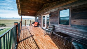 A wooden cabin with a wooden deck, a covered porch, and a view of the mountains.