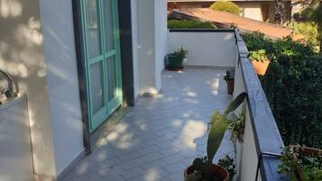 Un balcón con plantas en macetas, suelo de baldosas y vistas a edificios vecinos.
