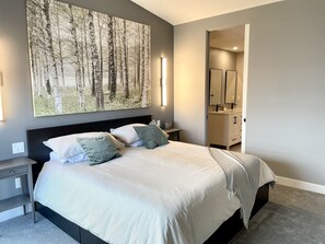 Et moderne soveværelse med en stor seng, sengeborde, et natbord og et stort maleri på væggen.