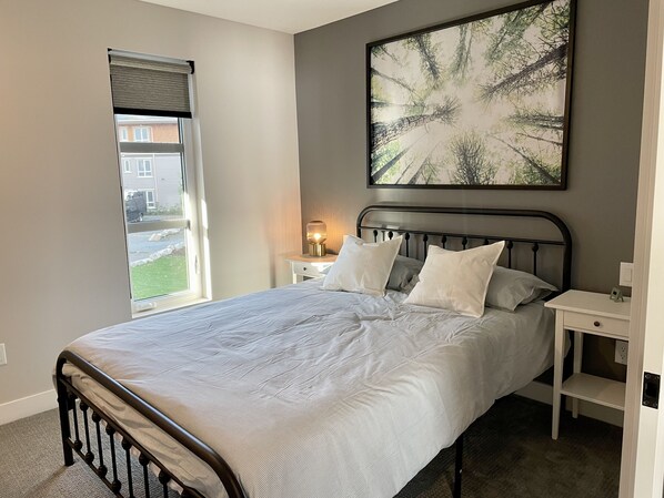 A bedroom with a bed, bedside tables, a window, and a painting on the wall.