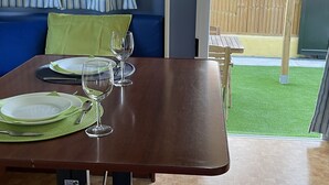 A dining area with a table set for two, a sofa, and a view of a wooden fence and grass outside. - Rural Mery (Mijas Golf)