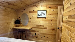 Una stanza accogliente in legno con un letto, una scrivania e uno specchio. Un cartello sulla parete recita “resta un PO'”.