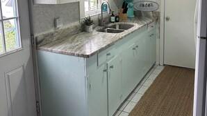 A kitchen with white cabinets, a sink, a countertop, a hanging light, and a clock on the wall. - Plum Island Quaint Getaway across from the beach (Newbury)