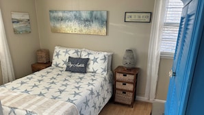 A bedroom with a bed featuring a star pattern, a bedside table with baskets, a wall art piece, and a sign on the wall. - Plum Island Quaint Getaway across from the beach (Newbury)