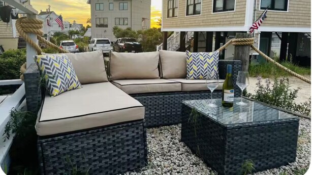 A modern outdoor seating area with a sofa and two side tables, surrounded by a garden setting. - Plum Island Quaint Getaway across from the beach (Newbury)