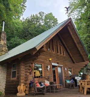 A log cabin with a sloped roof, a chimney, and a porch with wicker furniture. - Log Cabin next to the Mississippi River (Harpers Ferry)