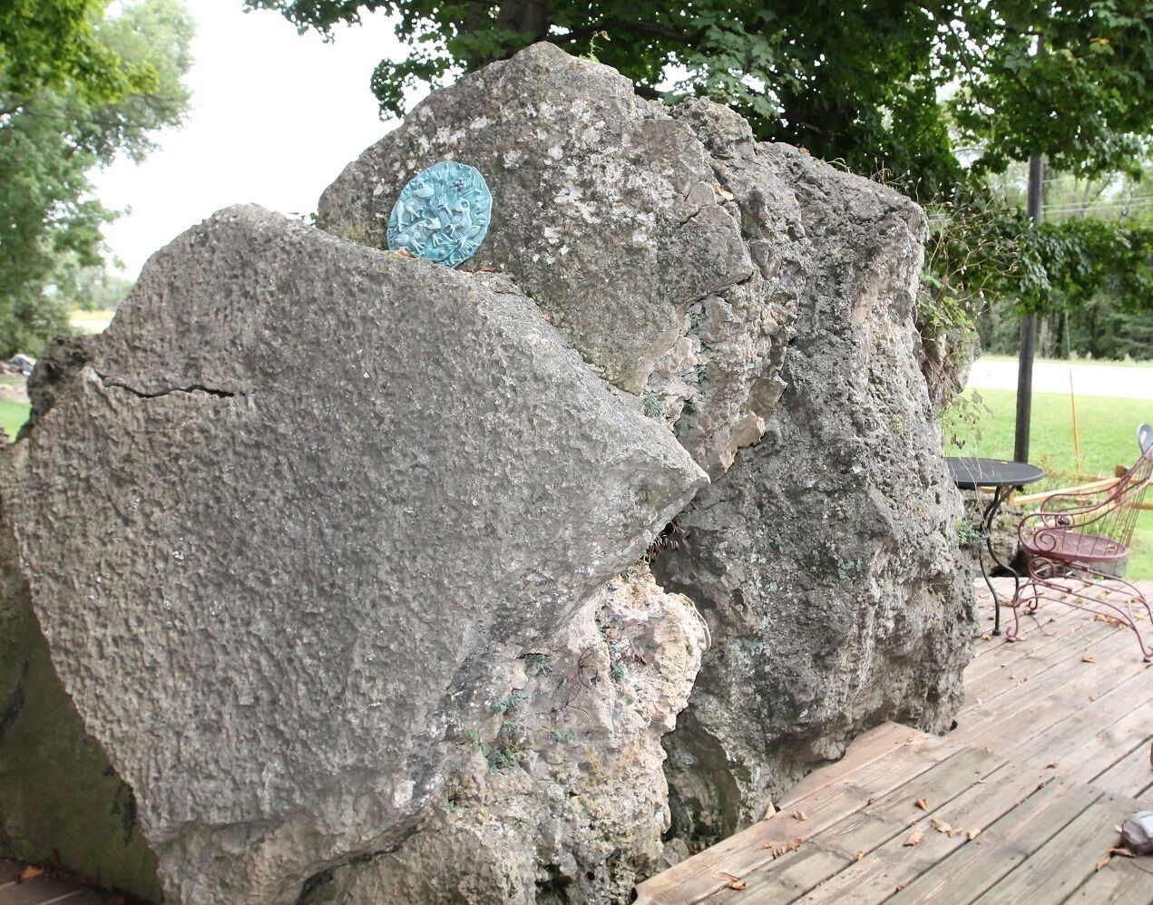 A large rock formation with a plaque, a wooden deck, and outdoor furniture.