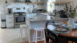 A modern kitchen with white cabinetry, a central island, and a dining area with a wooden table and chairs. - “Granite Getaway Cottage.”  An adorable cottage in a quiet family neighborhood (Granite Falls)