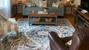 A living room with a ceiling fan, a clock, a sofa with cushions, a coffee table, a TV, and a fireplace. - “Granite Getaway Cottage.”  An adorable cottage in a quiet family neighborhood (Granite Falls)