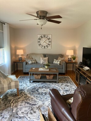 Relax in this inviting living space with a sofa, armchair, and TV on a stand.