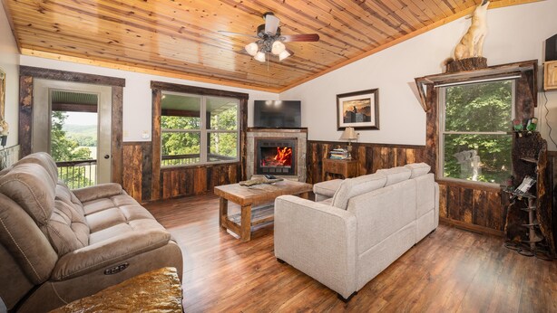 Ein gemütliches Wohnzimmer mit Kamin, Holzbalkendecke und großen Fenstern mit Blick ins Freie.